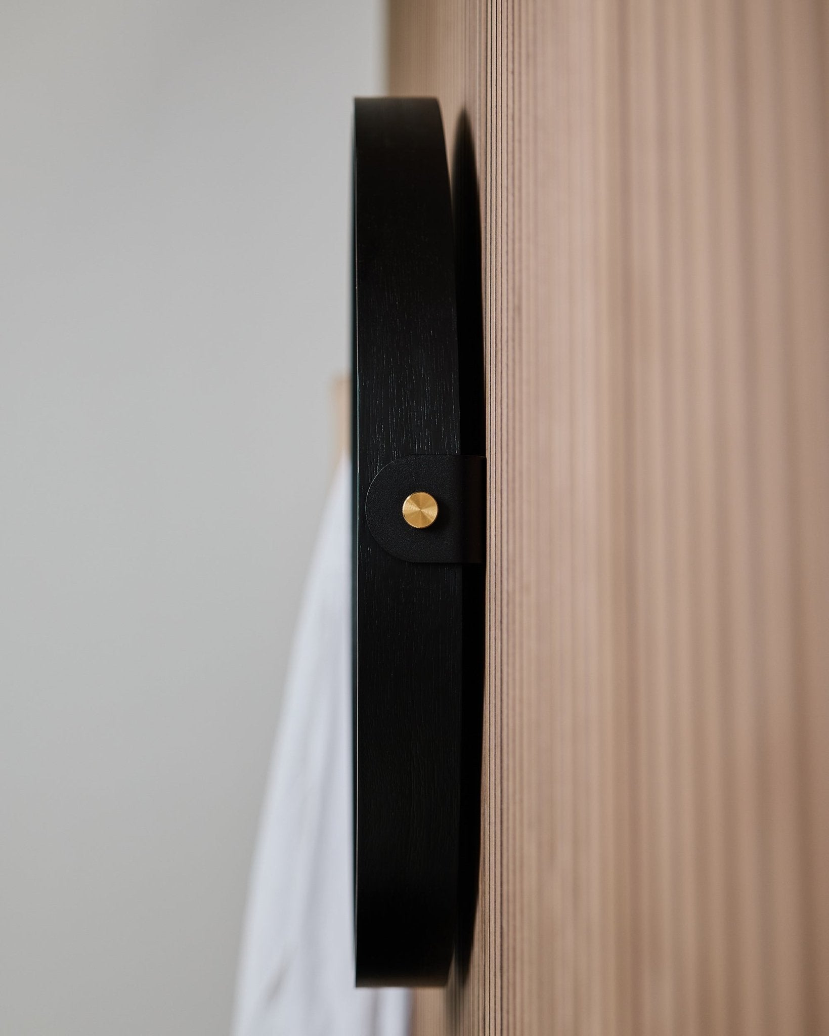 Close-up side view of the WoodUpp Linn | Mirror / Black Oak wall hook, mounted on a grooved oak acoustic panel, designed for hanging a round mirror.