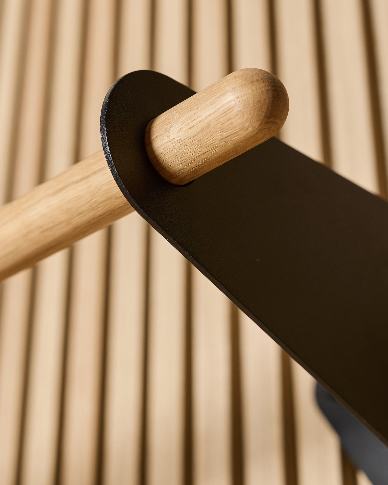 Close-up of the WoodUpp Linn Coat Rail in black, 75.9 cm, with a solid oak rod mounted in a black metal bracket on a Nordic acoustic slatwall panel.