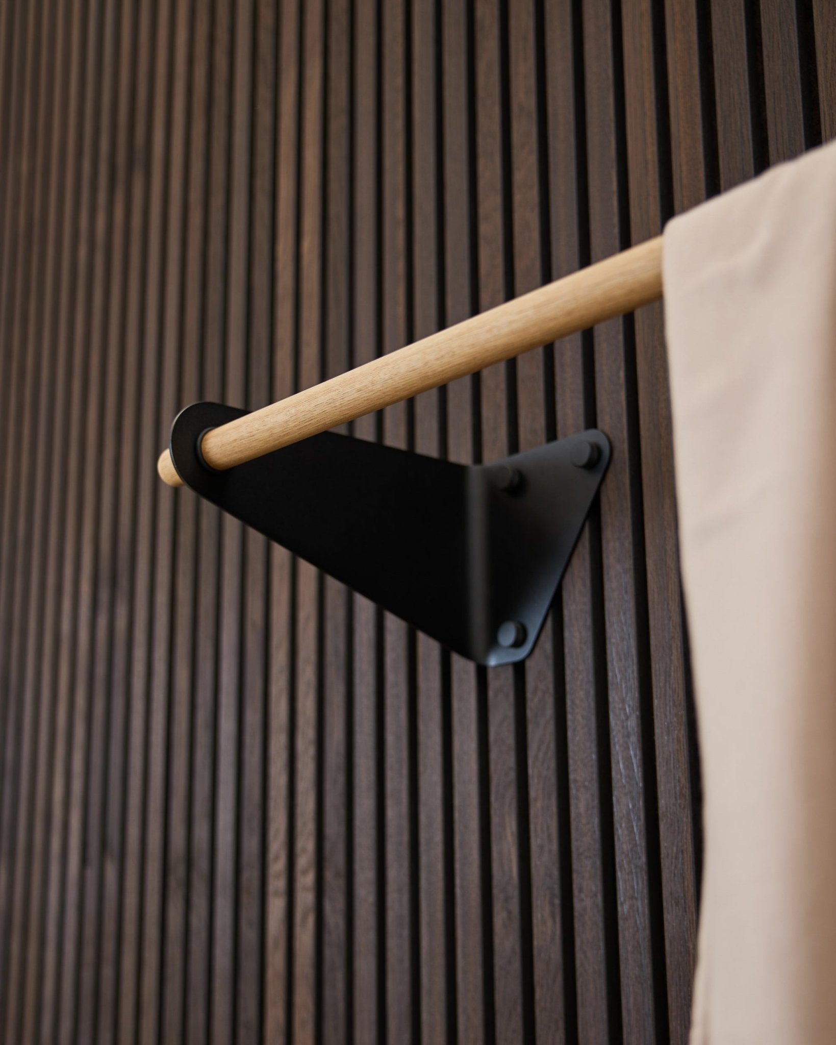 Linn Coat Rail by WoodUpp in black (115.9 cm) mounted on a dark grooved Akupanel acoustic panel, with beige fabric accent and black bracket.