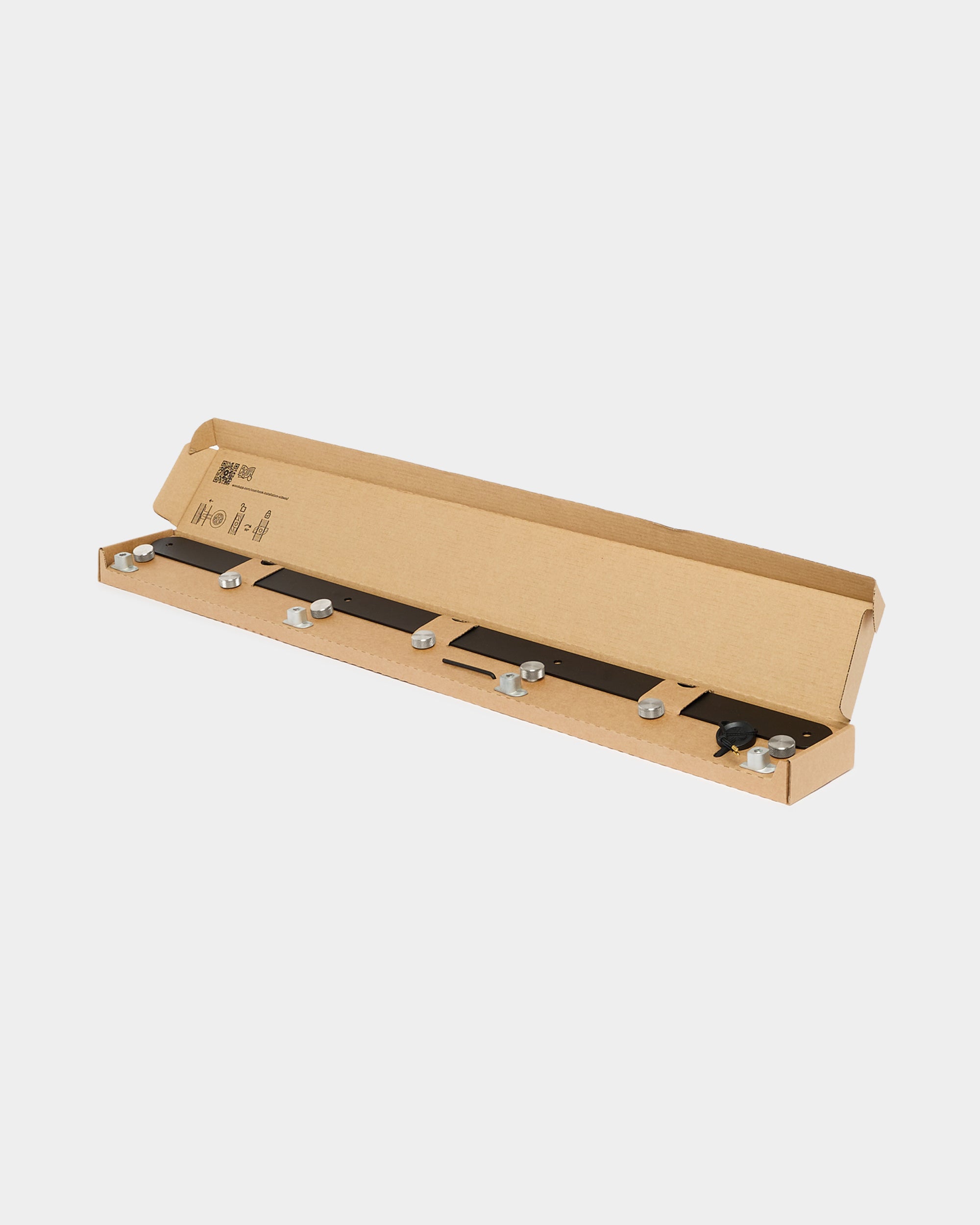 A long cardboard box contains a black metal bar with bolts and washers, components for assembling or installing a WoodUpp acoustic panel or room divider.
