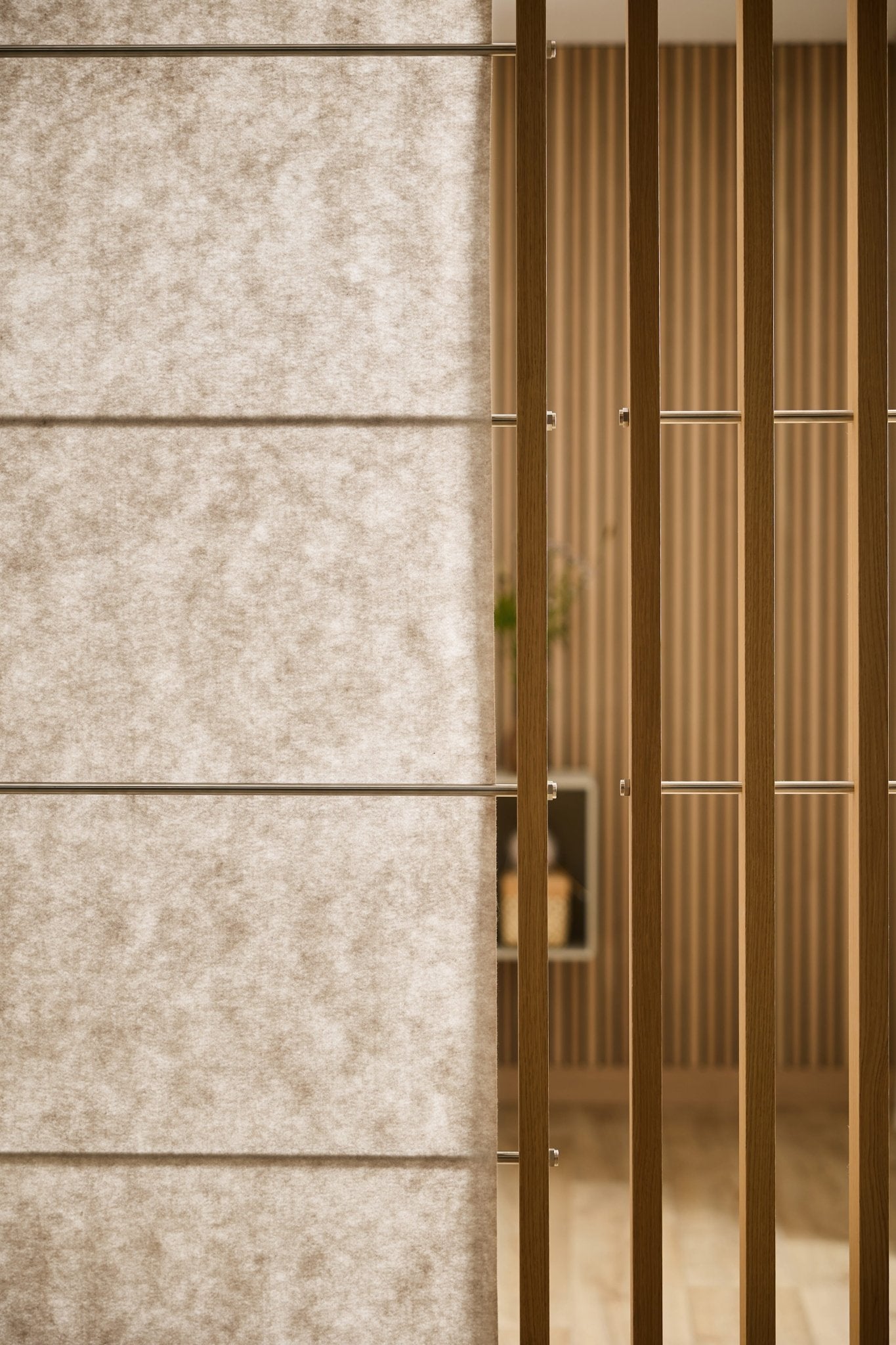 Close-up of WoodUpp Vigg Felt Sheet (58x176 cm, light beige) acoustic panel with vertical wood slats; blurred striped wallpaper and shelf in background.