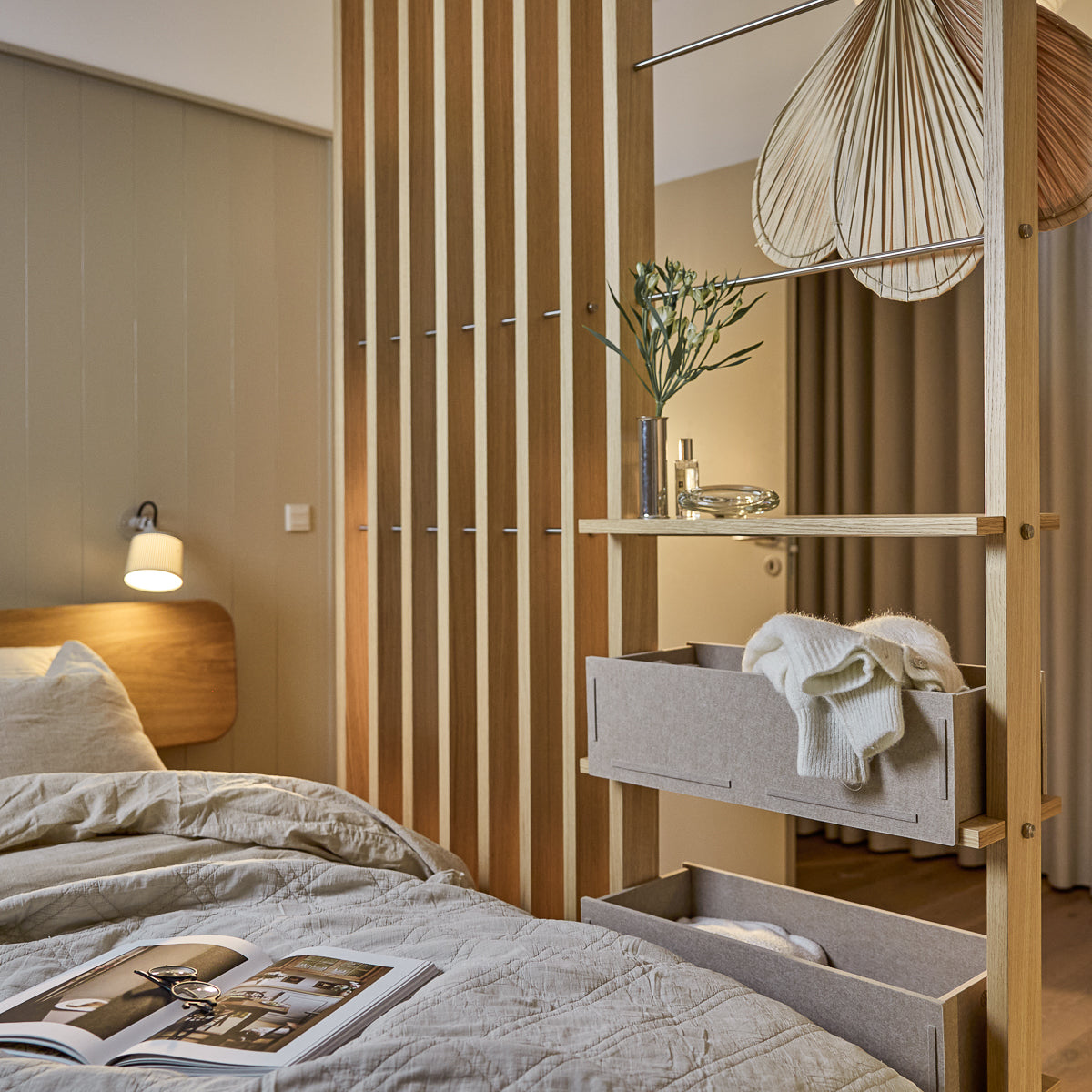 A modern bedroom with Nordic soft bedding, pendant lamp, and a magazine on the neatly made bed. WoodUpp Akupanel acoustic wood panels accent the wall.