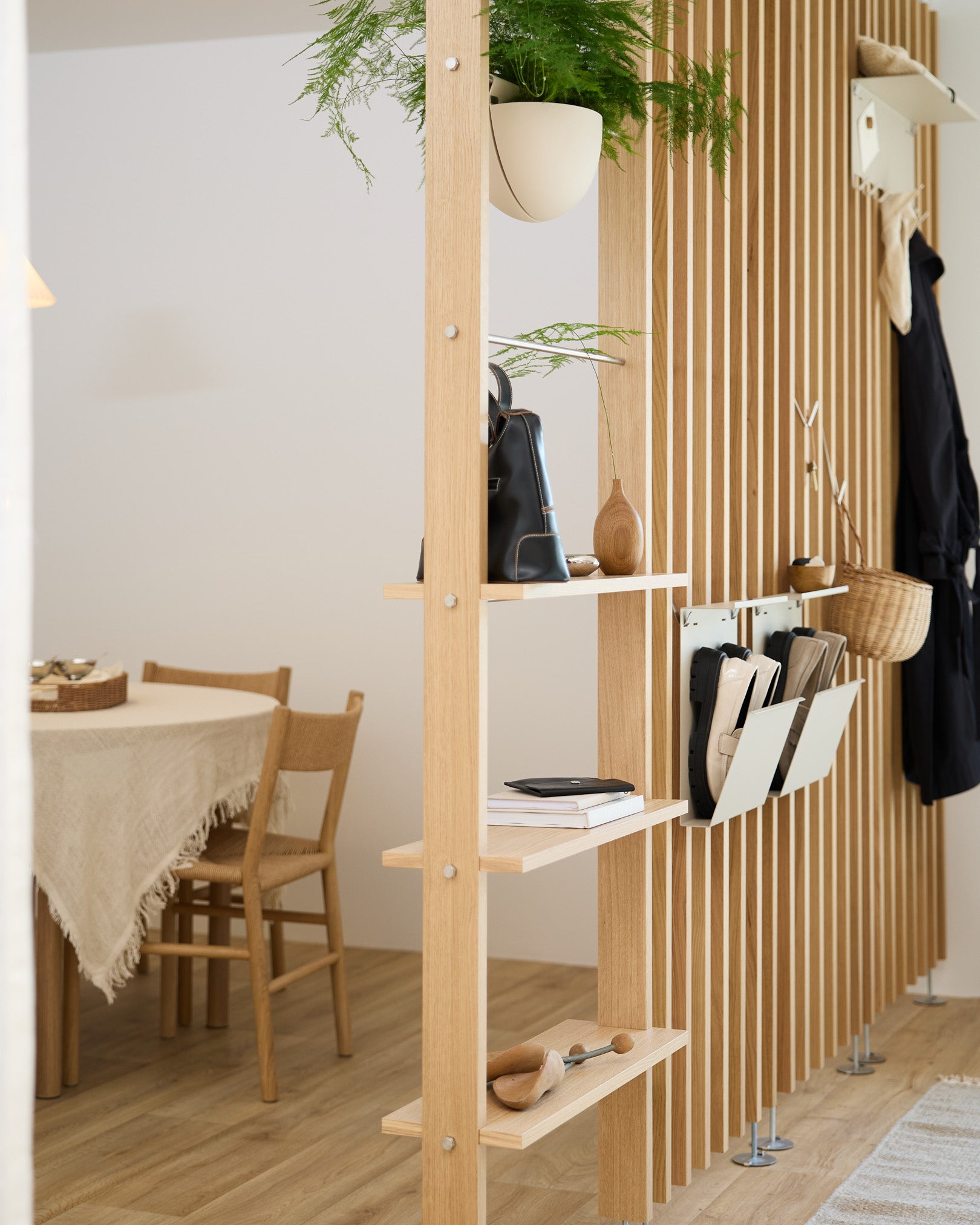Open wooden shelving divides the dining area, featuring Nell Shoe Storage in beige by WoodUpp for organized shoe space in a modern Nordic home.