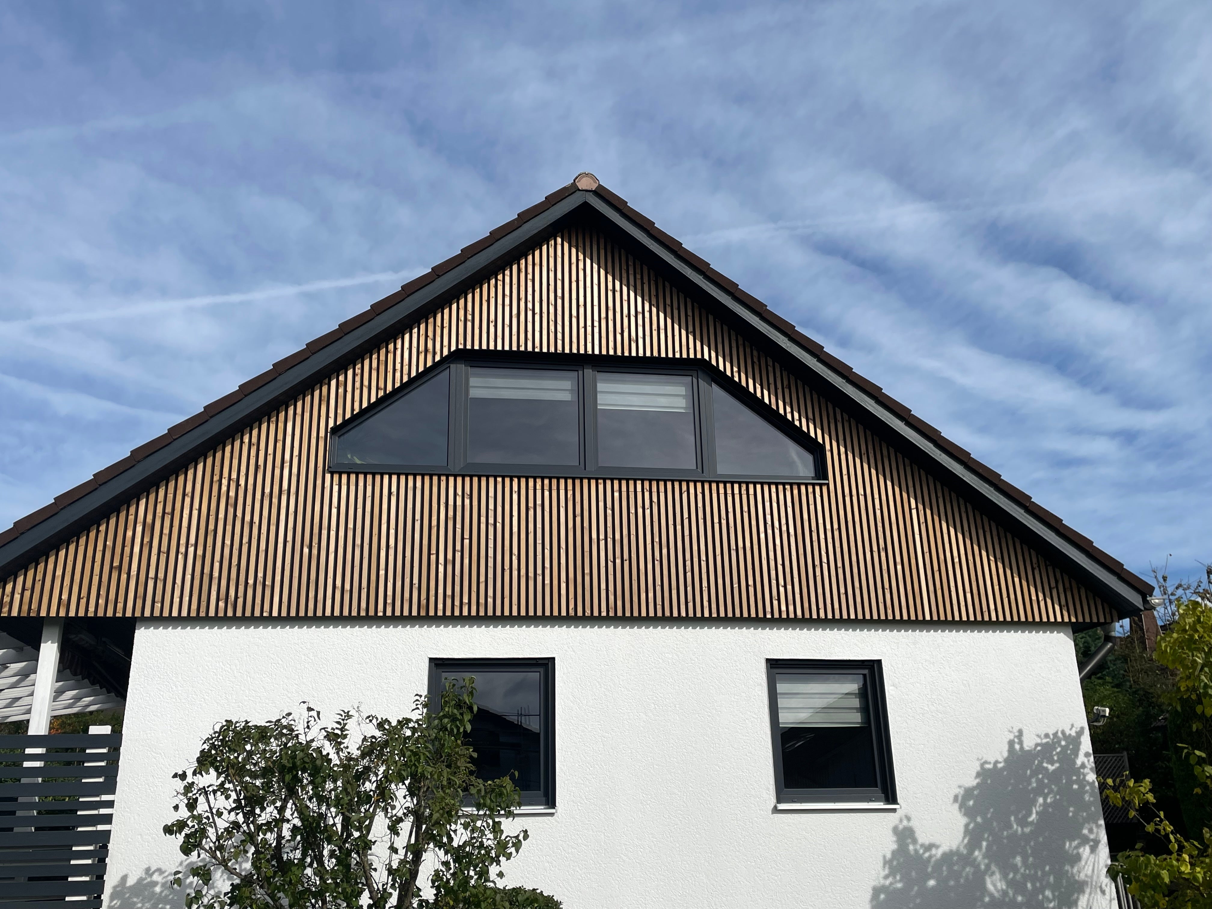 Aluwood aluminium slat cladding on gable above white rendered wall and black-framed windows.