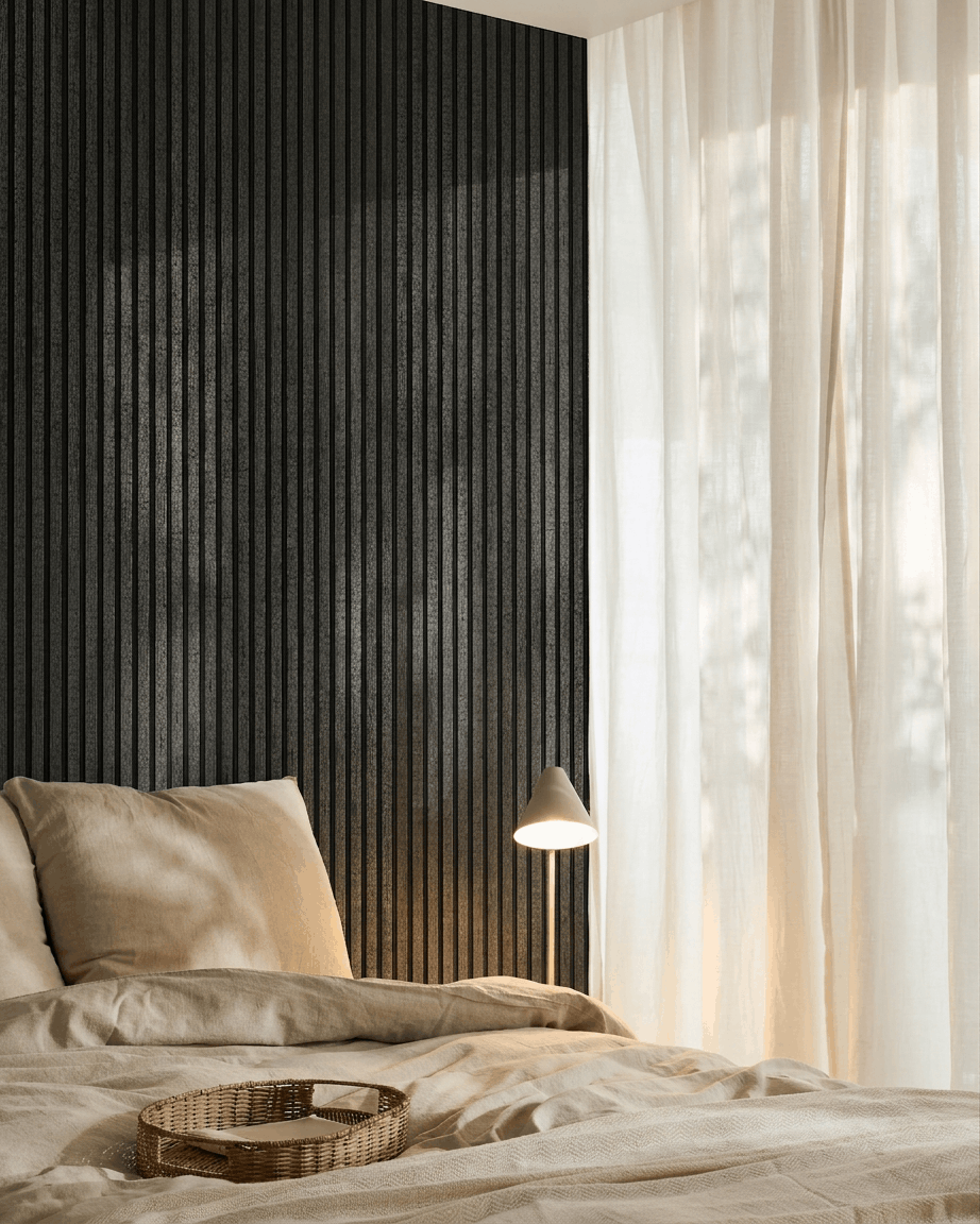 Cozy bedroom with beige bedding, a rattan tray, white lamp, sheer curtains, and a WoodUpp Akupanel charcoal acoustic wood panel mounted on the wall.