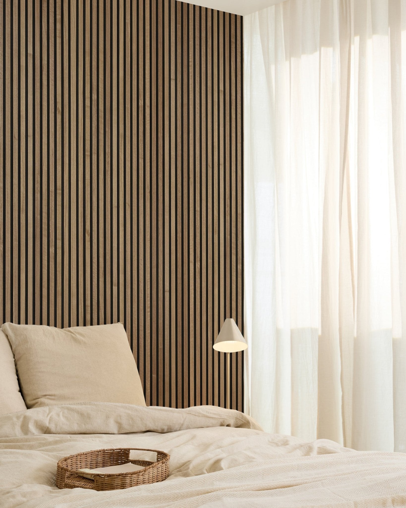 Minimalist bedroom featuring a WoodUpp Original Akupanel Walnut acoustic panel (240x60cm) on the wall, beige bedding, sheer curtains, woven tray, and small wall lamp.
