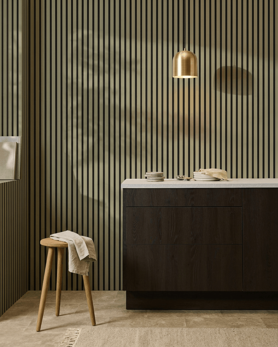 Modern kitchen with dark wood cabinets, marble countertop, brass pendant lamp, and a WoodUpp Akupanel Colored acoustic slatwall panel for sound absorption.