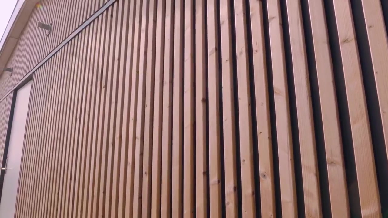 Low-angle view along a wall of vertical Aluwood slats with a white door and a round vent
