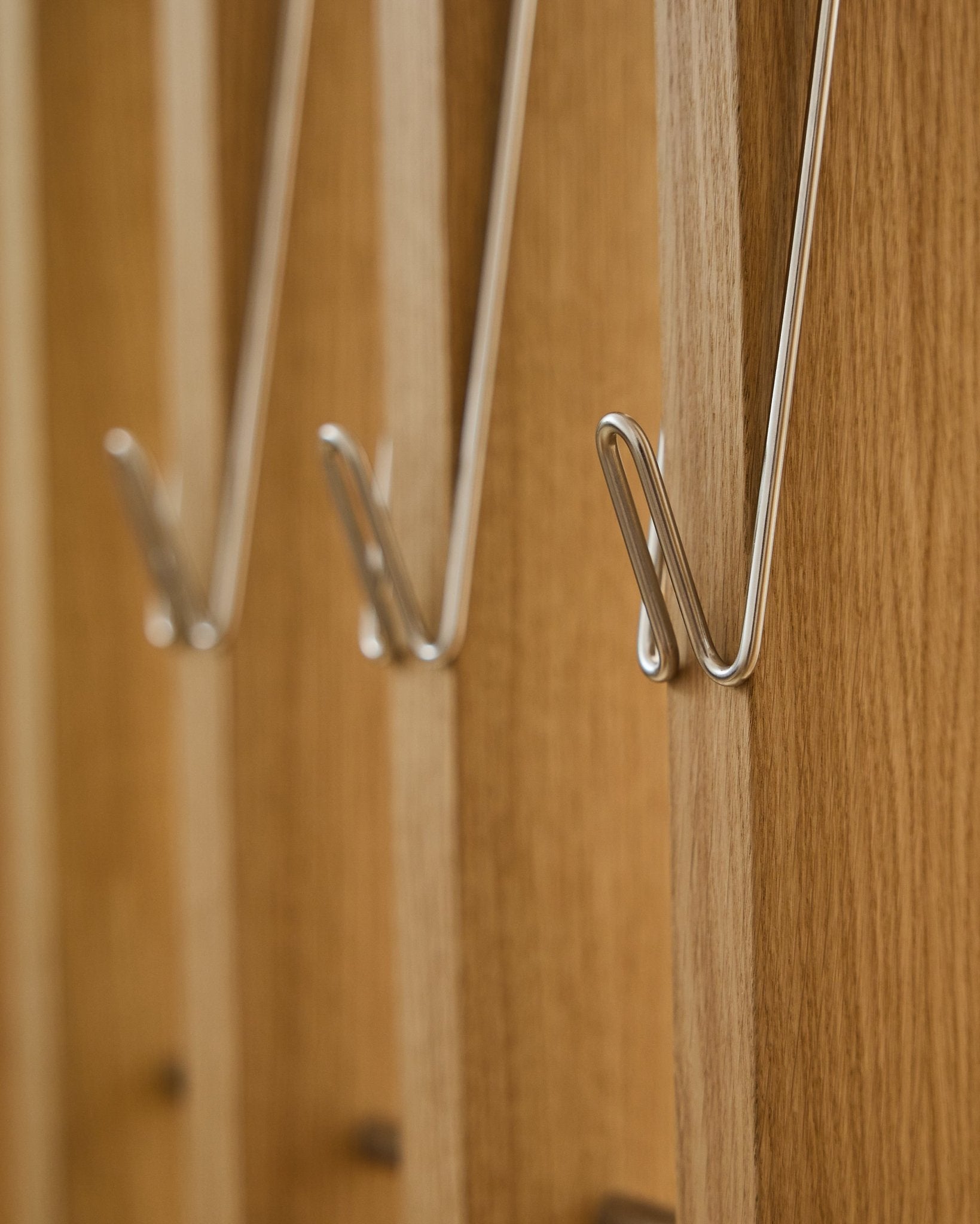 Close-up of three Alva | Wire Hook / BM1, Stainless Steel, Long by WoodUpp, mounted in a row on Akupanel acoustic wood panels and casting soft shadows.